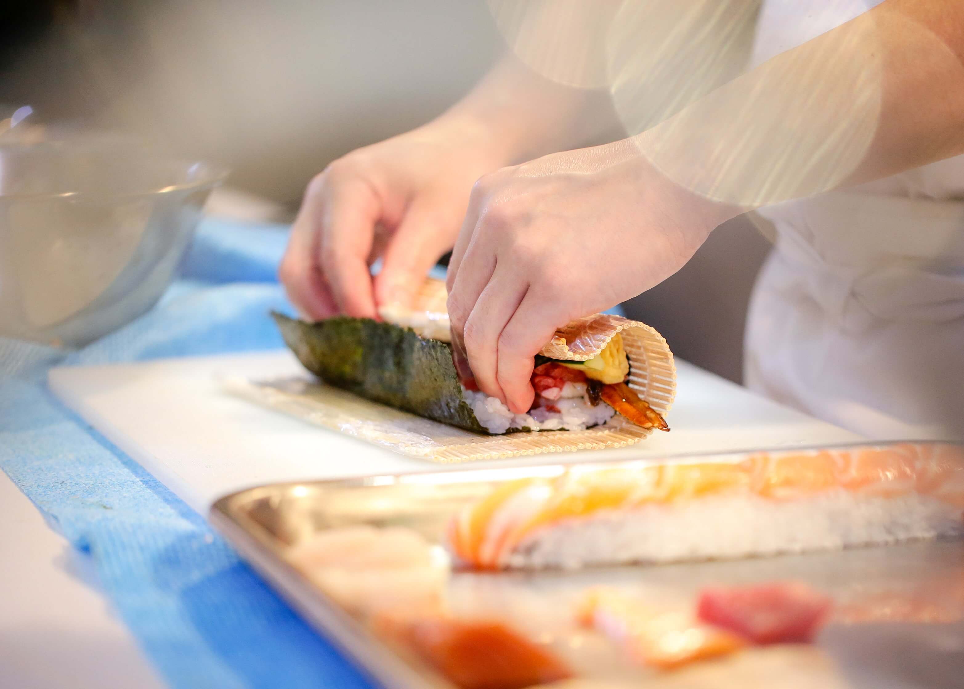 Hände rollen ein Futomaki auf einer Bambusmatte